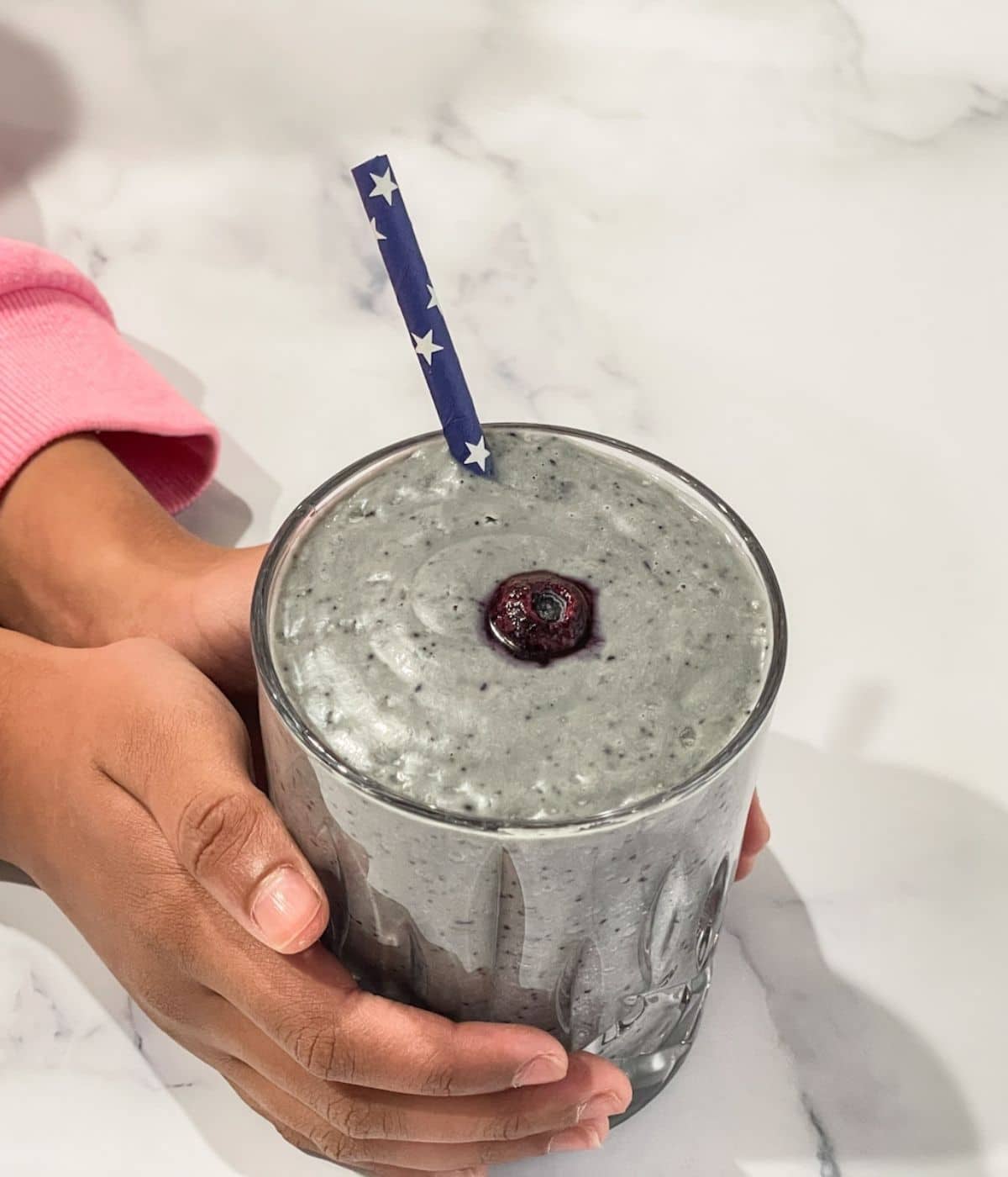 A girl hand is holding avocado blueberry banana smoothie.