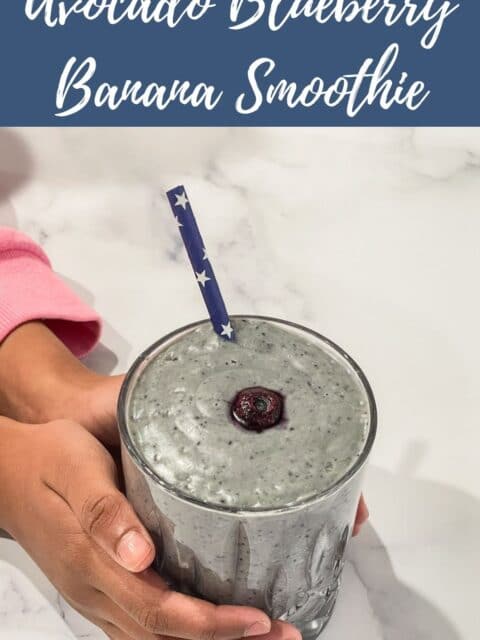 A girl hand is holding up avocado blueberry smoothie glass.