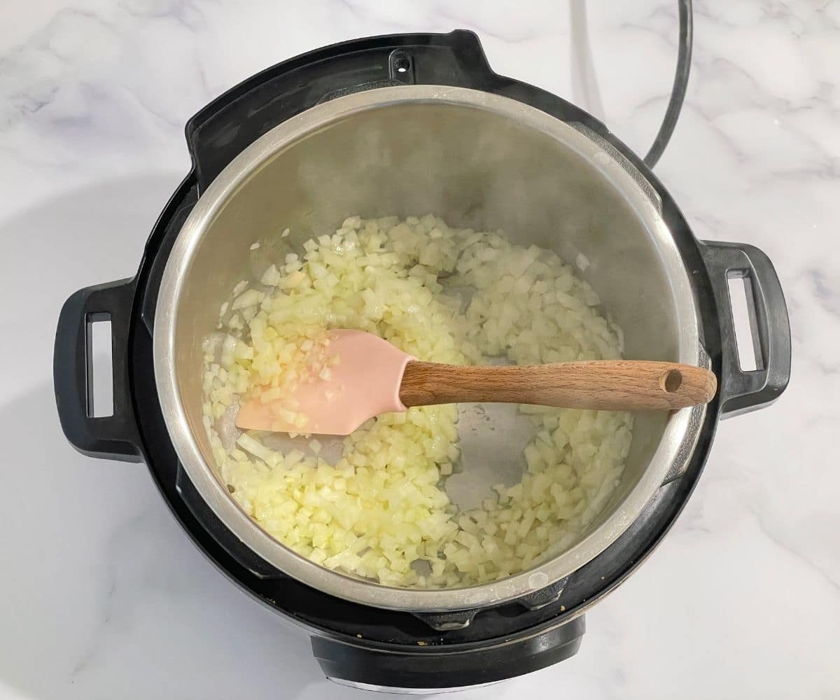 An instant pot is with garlic and chopped onion on saute mode.