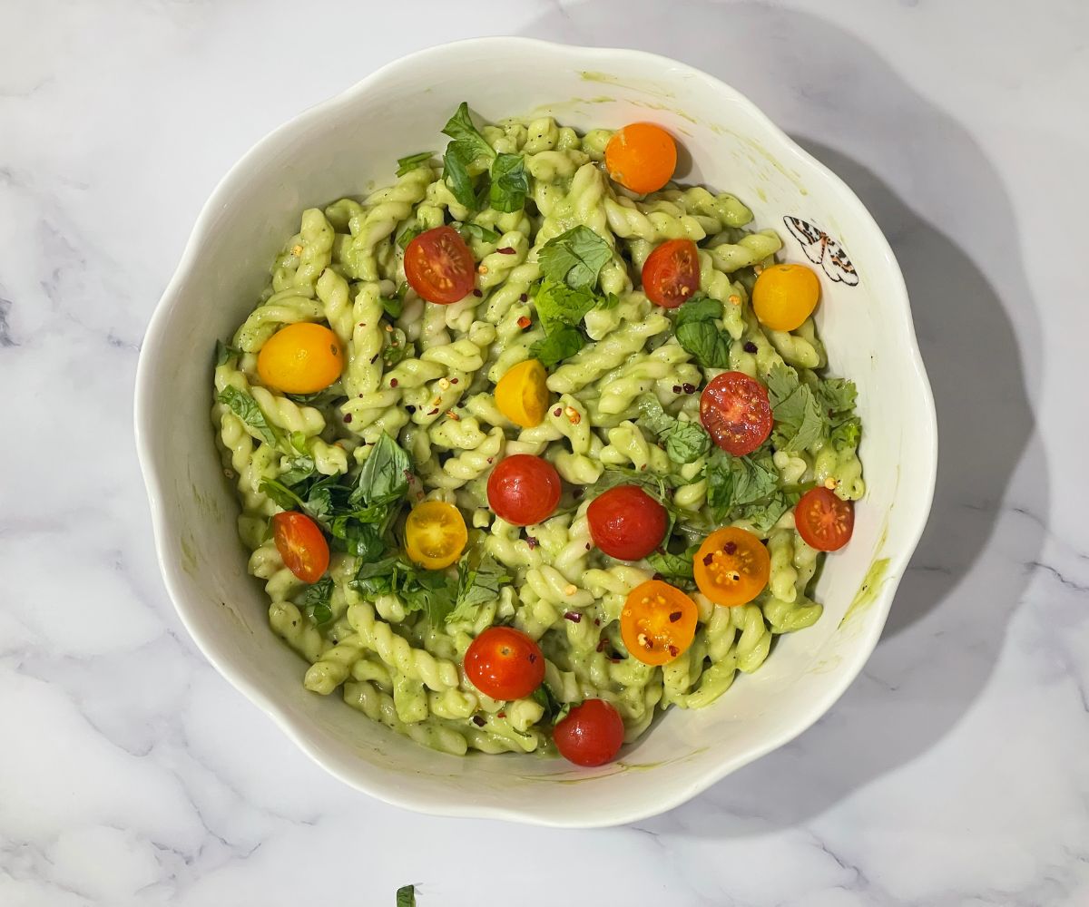 A bowl of vegan Avocado pasta and topped with chopped cilantro and cherry tomatoes.