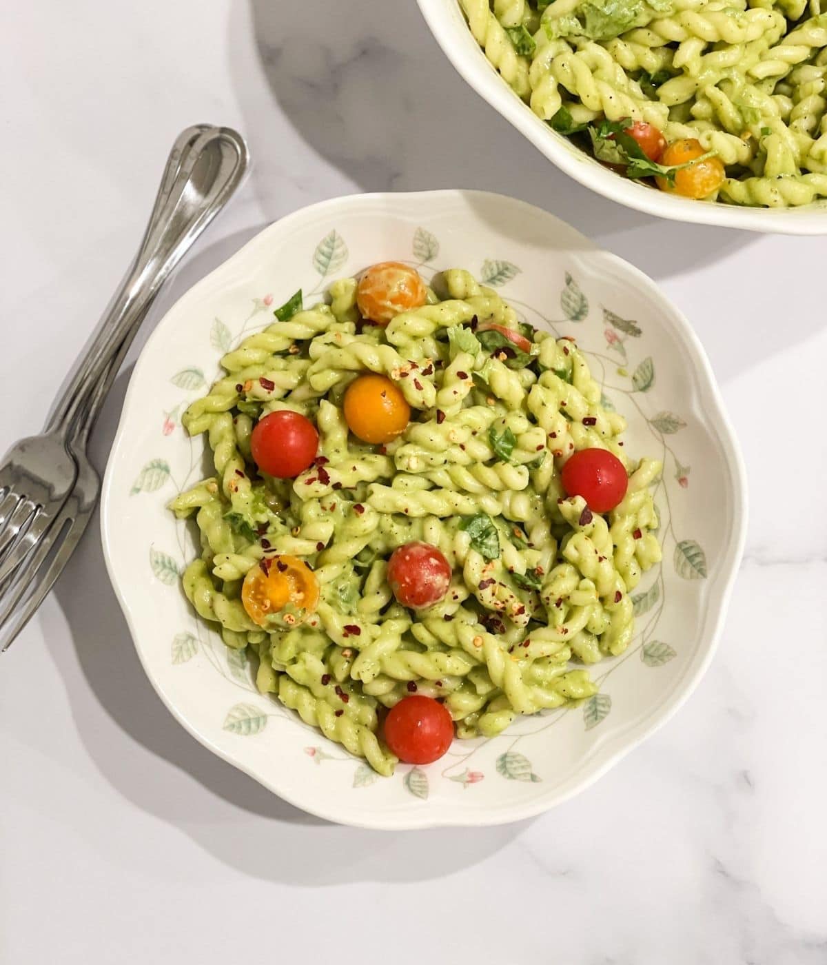 A plate is filled with avocado pasta and topped with cherry tomatoes.