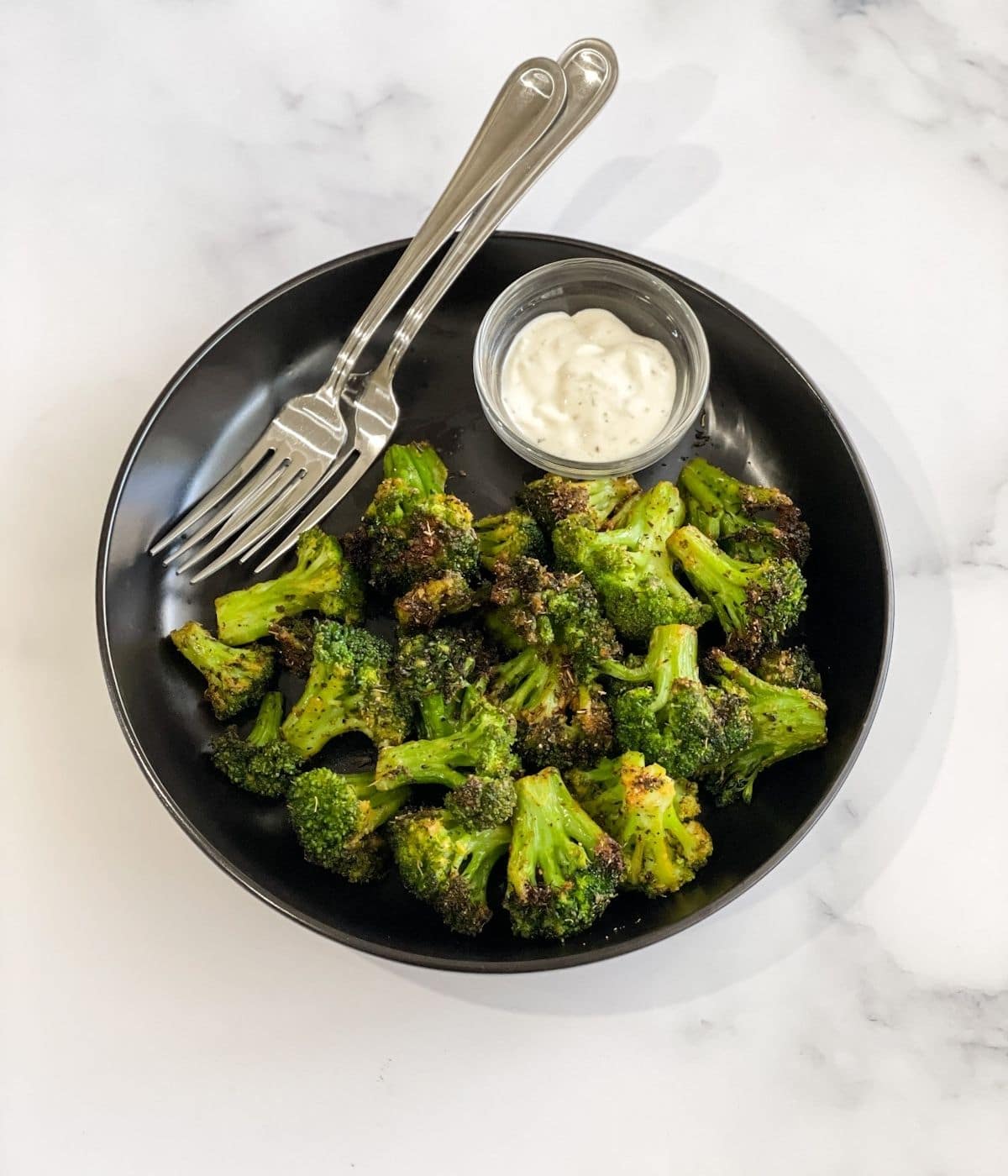 A plate of air fried broccoli is on the table with vegan ranch dressing and fork.