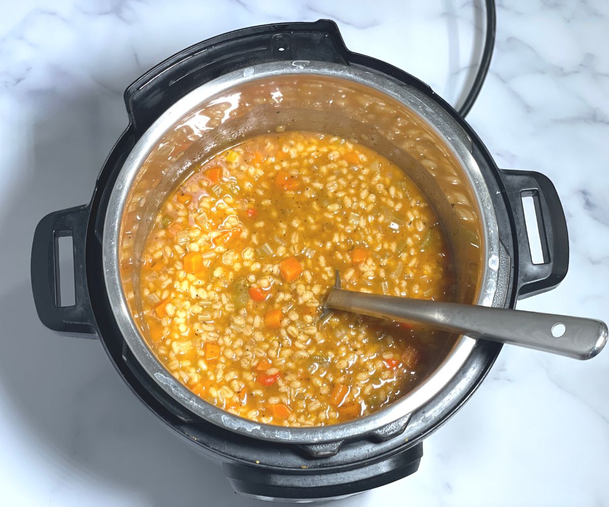 An instant pot is with warm vegetable barley soup.