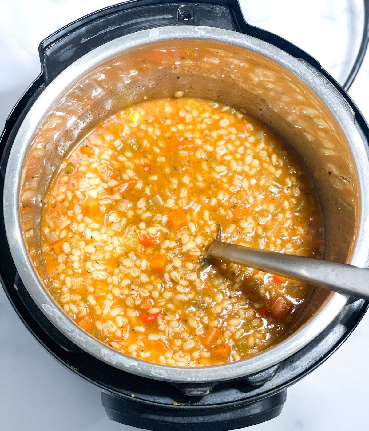 A pot of vegetable barley soup is on the table with big spoon.