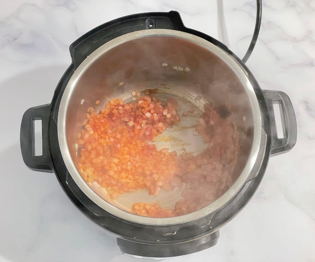 An instant pot is with tomato paste and onions on cook mode.