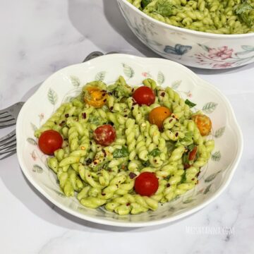 A plate of vegan avocado pasta is on the table along with fork by the side.