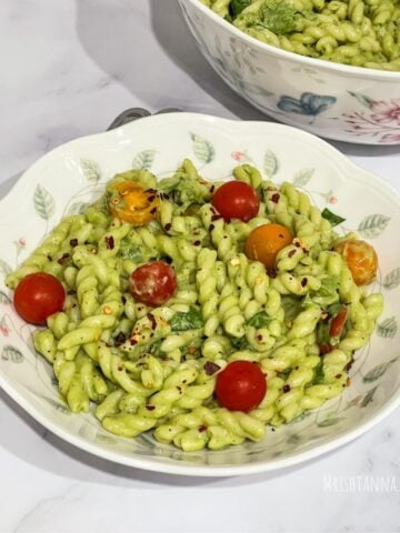 A plate of vegan avocado pasta is on the table along with fork by the side.