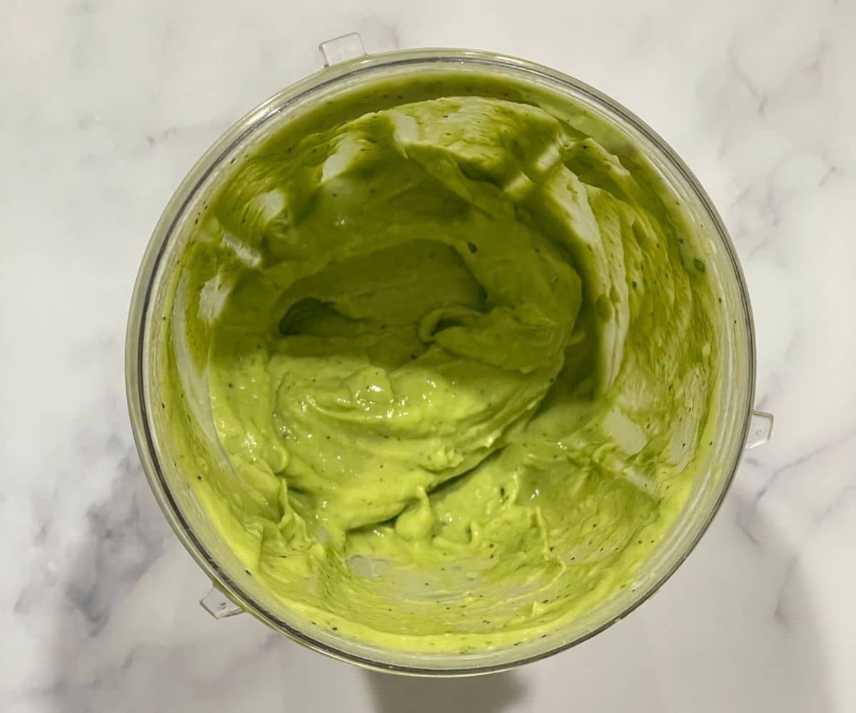 a blender is filled with creamy avocado pasta sauce on the table.