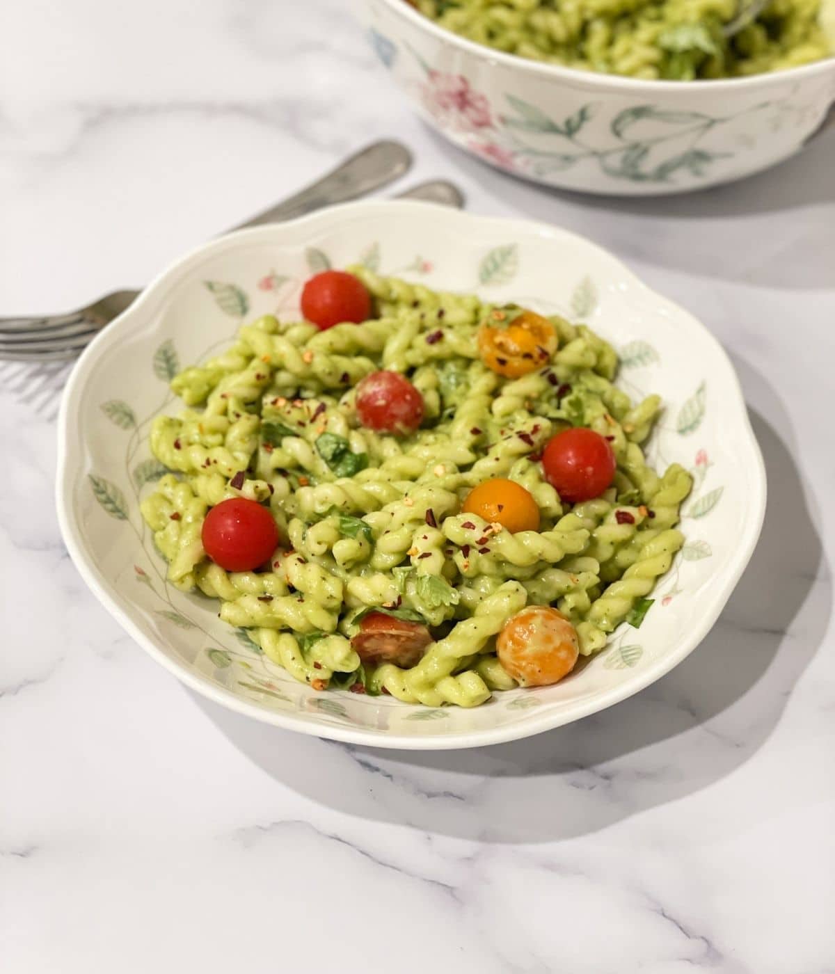 A plate of creamy avocado pasta is on the table with fork on the side.