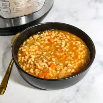 A bowl of barley soup is on the table with golden spoon.