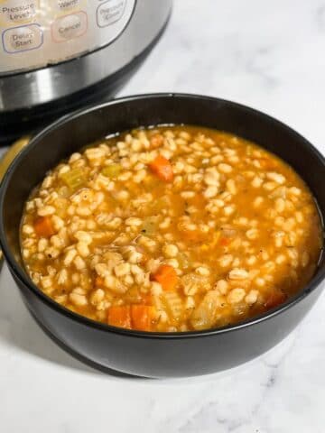 A bowl of barley soup is on the table with golden spoon.