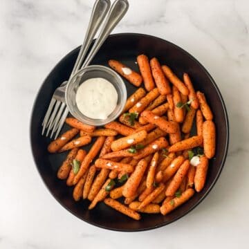 A plate of roasted carrots are on the table.