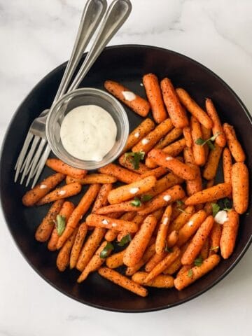 A plate of roasted carrots are on the table.