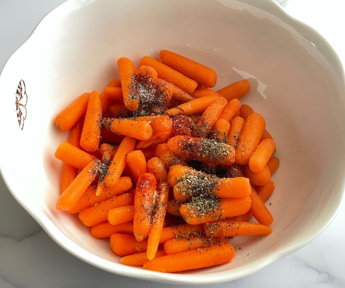 A bowl is with baby carrots and seasonings.