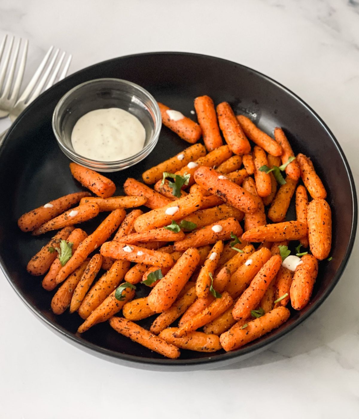 A plate of air fryer baby carrots are with vegan ranch.