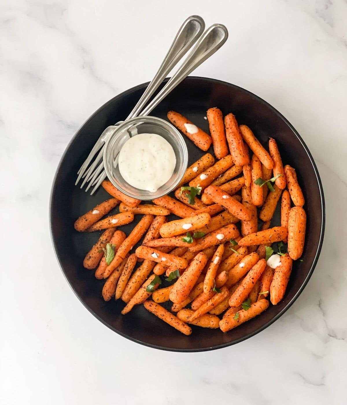 A plate is with roasted baby carrots on the table with fork.