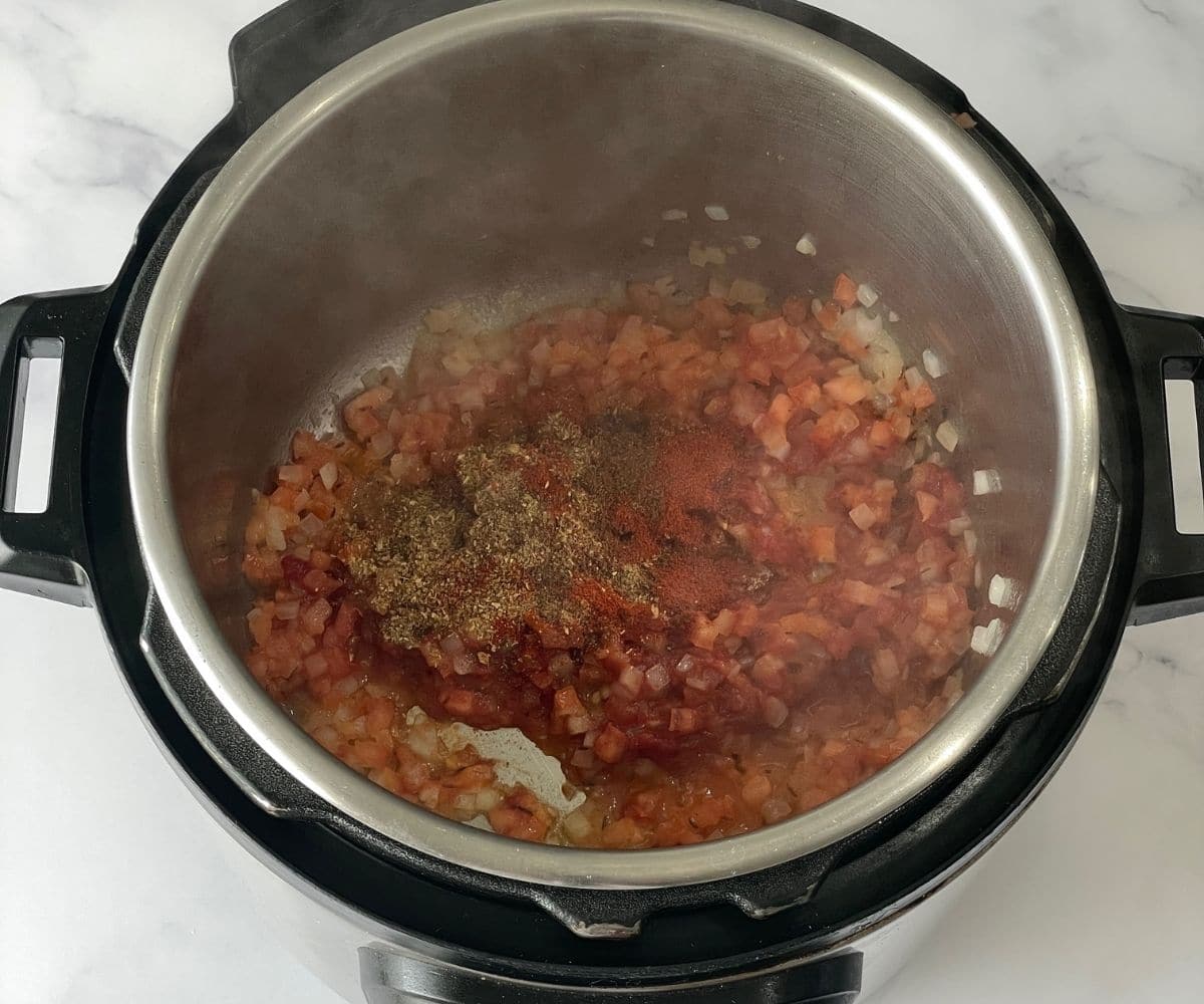 An instant pot is with tomatoes and spices.