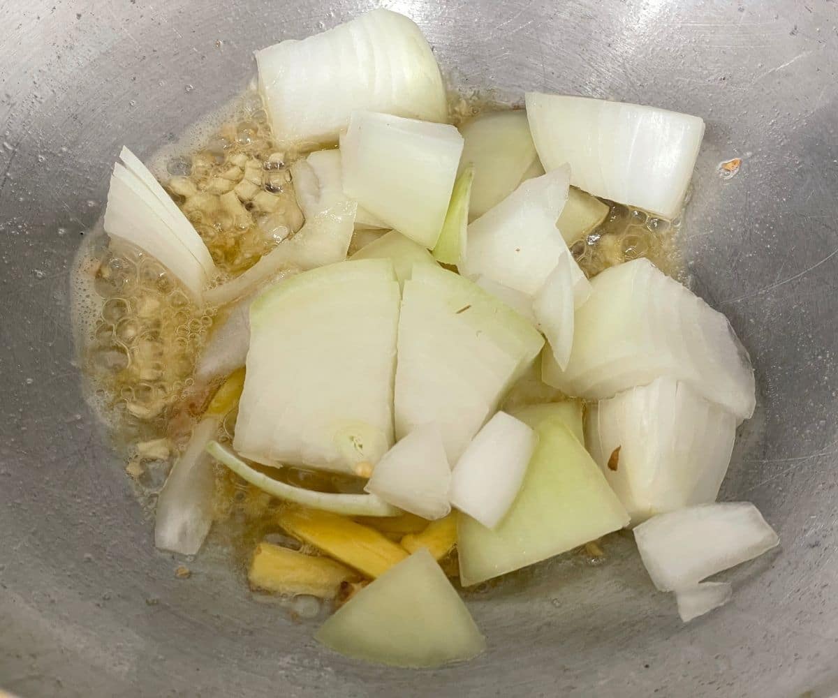 A kadai is with onion, ginger over the stove top.