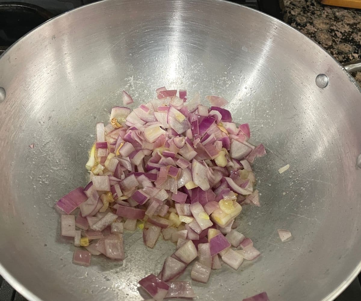 A kadai is with garlic and onions over the heat.