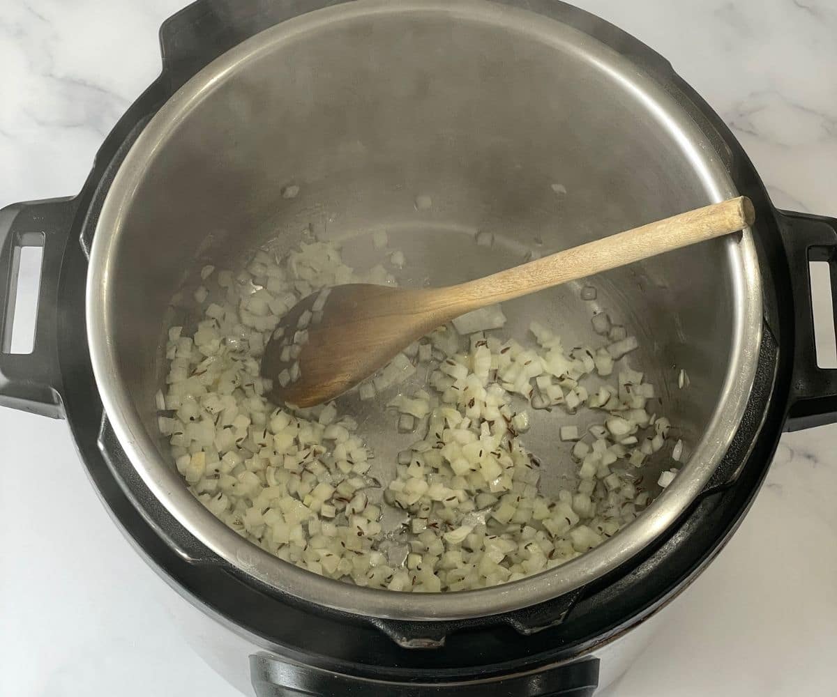 An instant pot is with onions and spices on saute mode.