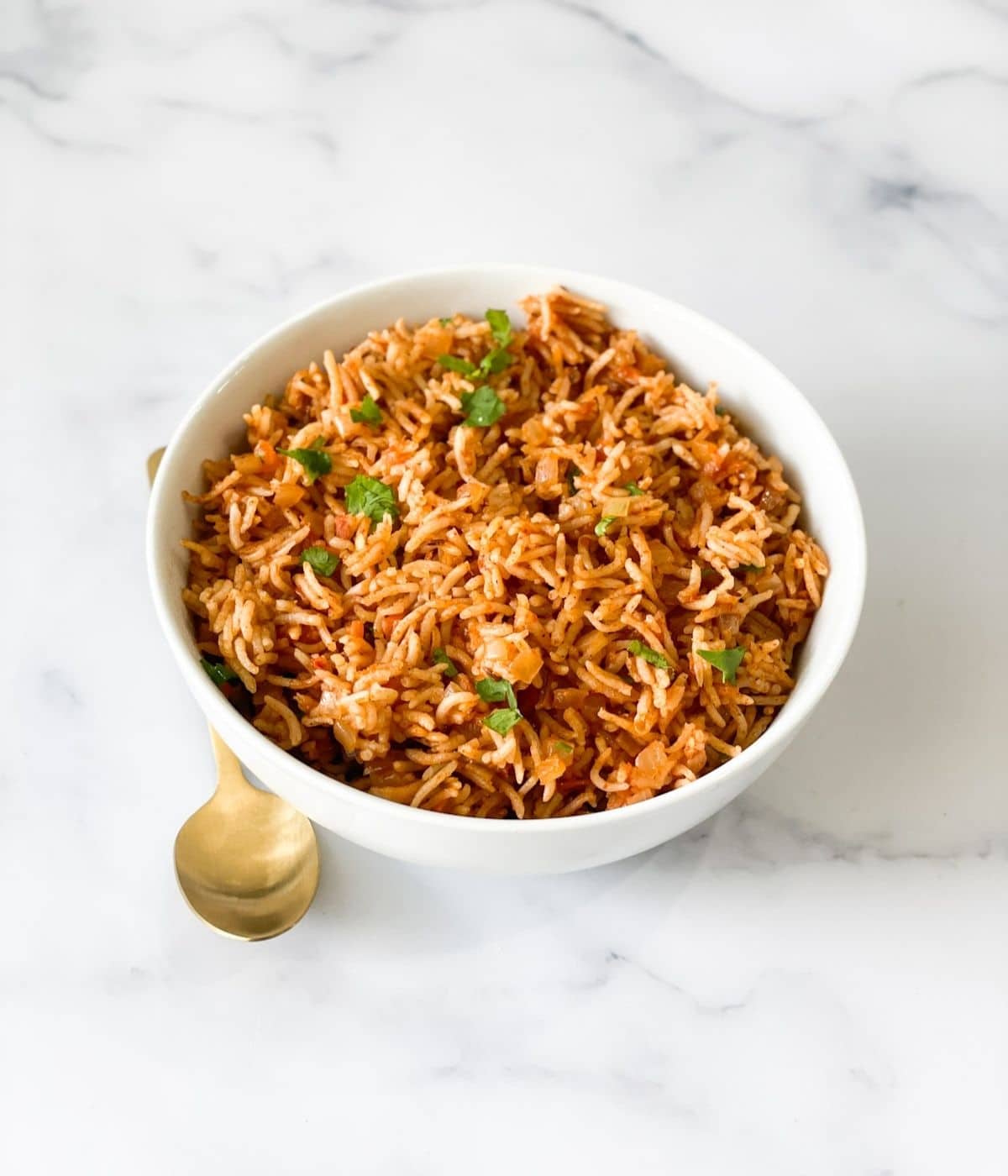 A bowl of tomato rice is on the table with golden spoon.