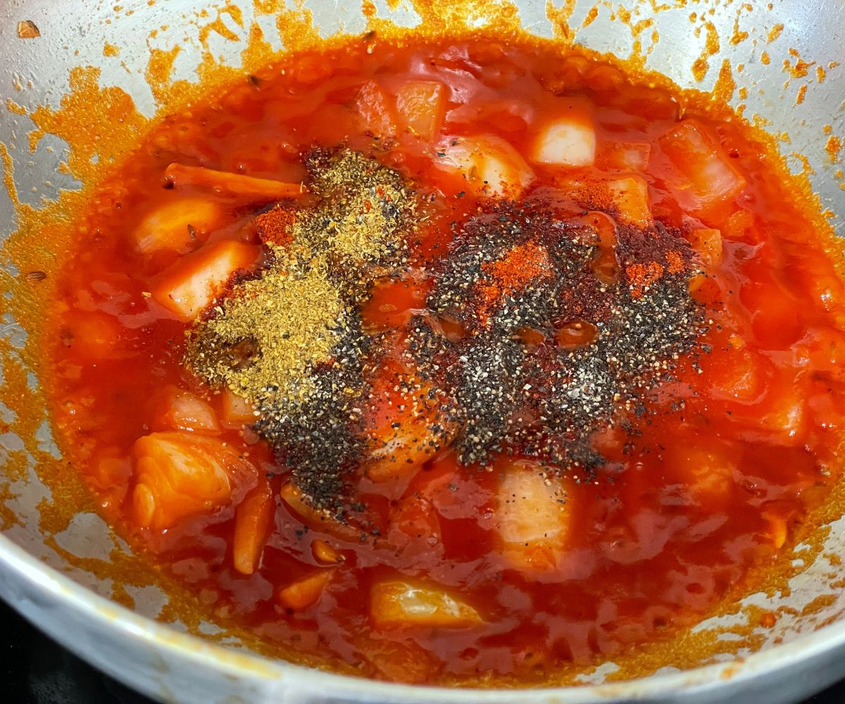 A large pan is with tomato sauce and spices over the heat.