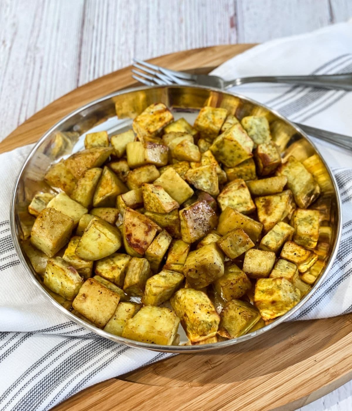 A silver plate is with air fried sweet potato cubes.