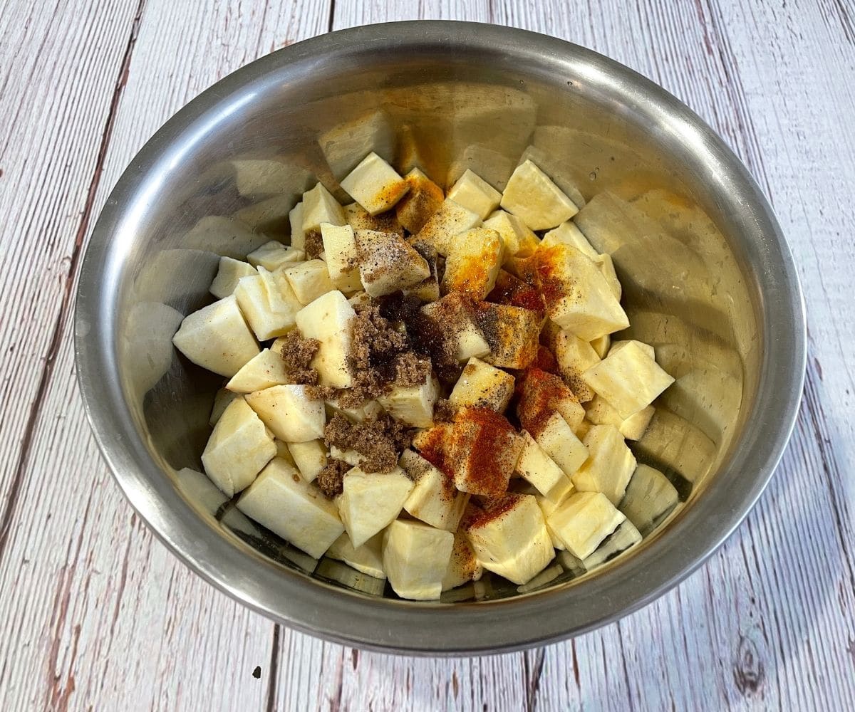 A large bowl is with sweet potato cubes and spices.