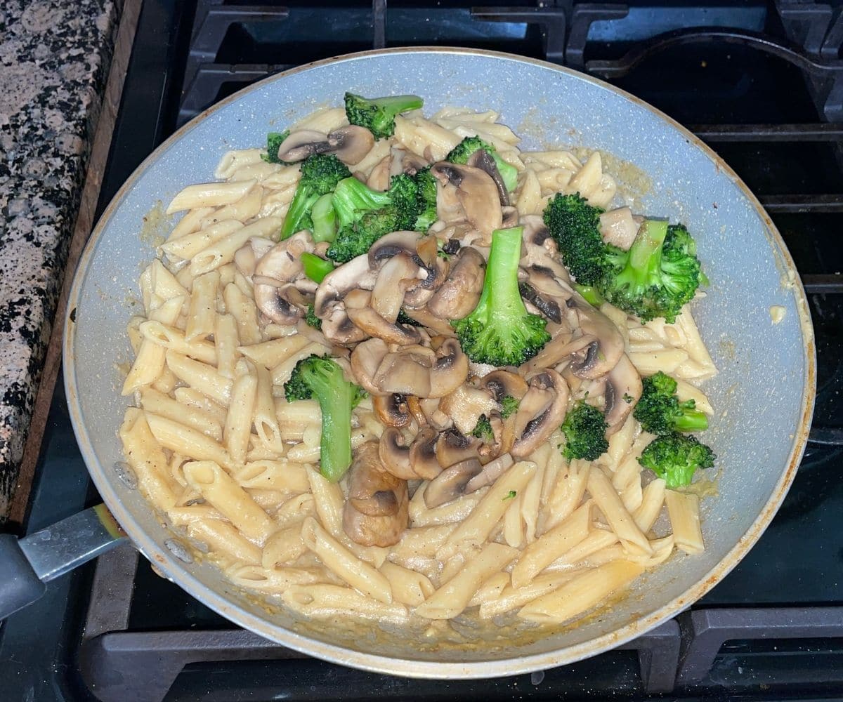 A pan is with pasta, broccoli and mushroom.