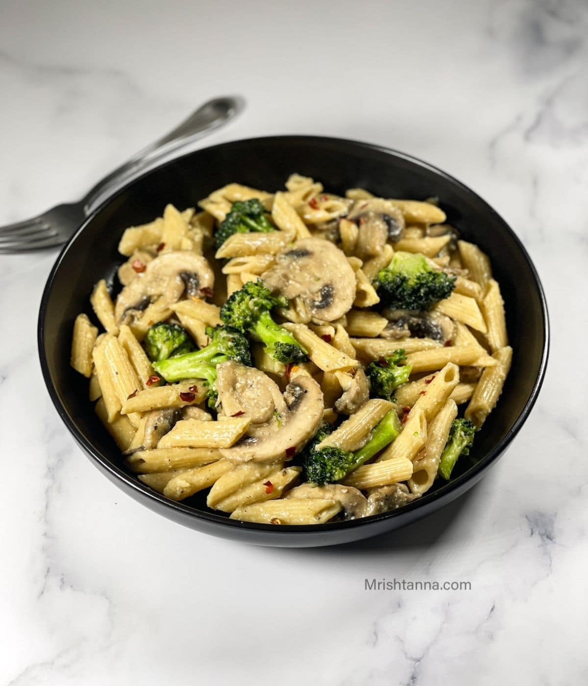 A bowl of vegan creamy mushroom pasta is on the table with a fork.