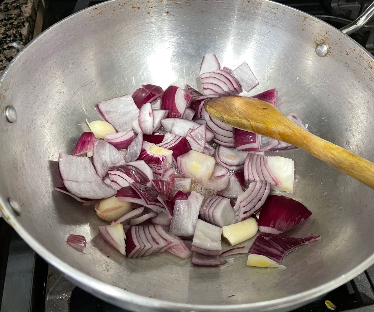 A kadai is with onions and garlic over the heat.