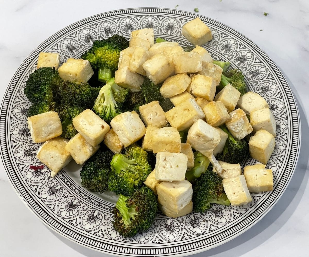 A plate is with air fried broccoli and tofu.