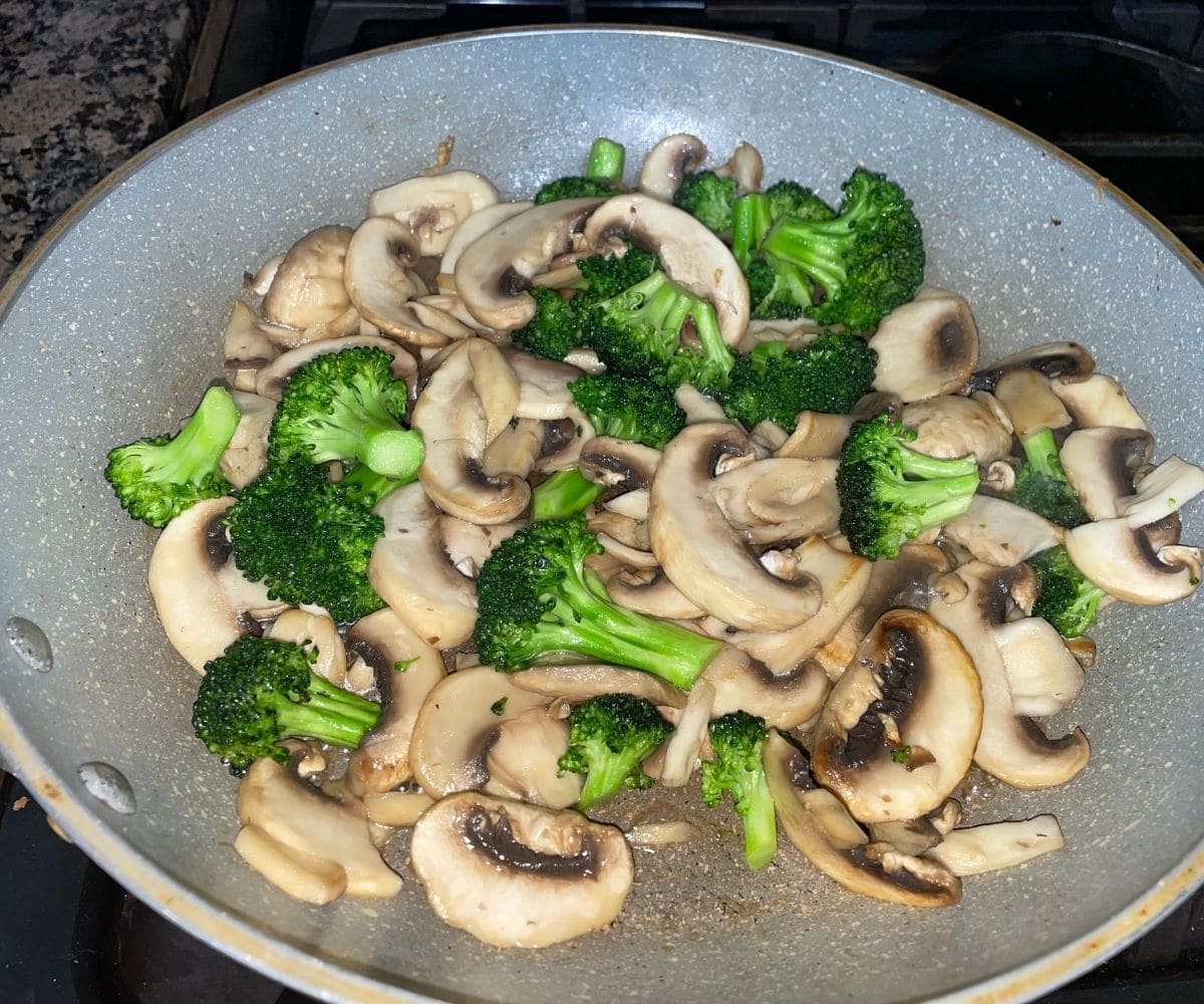 A pan is with mushrooms and broccoli florets over the heat.