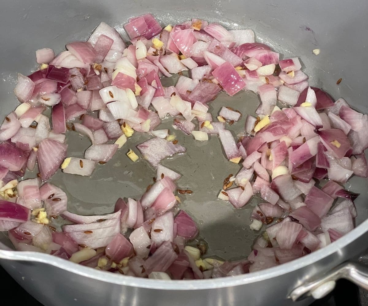 A pan is with cumin seeds, and chopped onions over the heat.