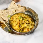 A copper bowl is with cabbage curry and chapati on side.