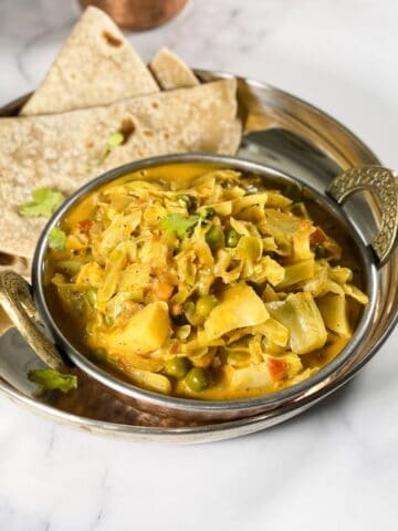 A copper bowl is with cabbage curry and chapati on side.