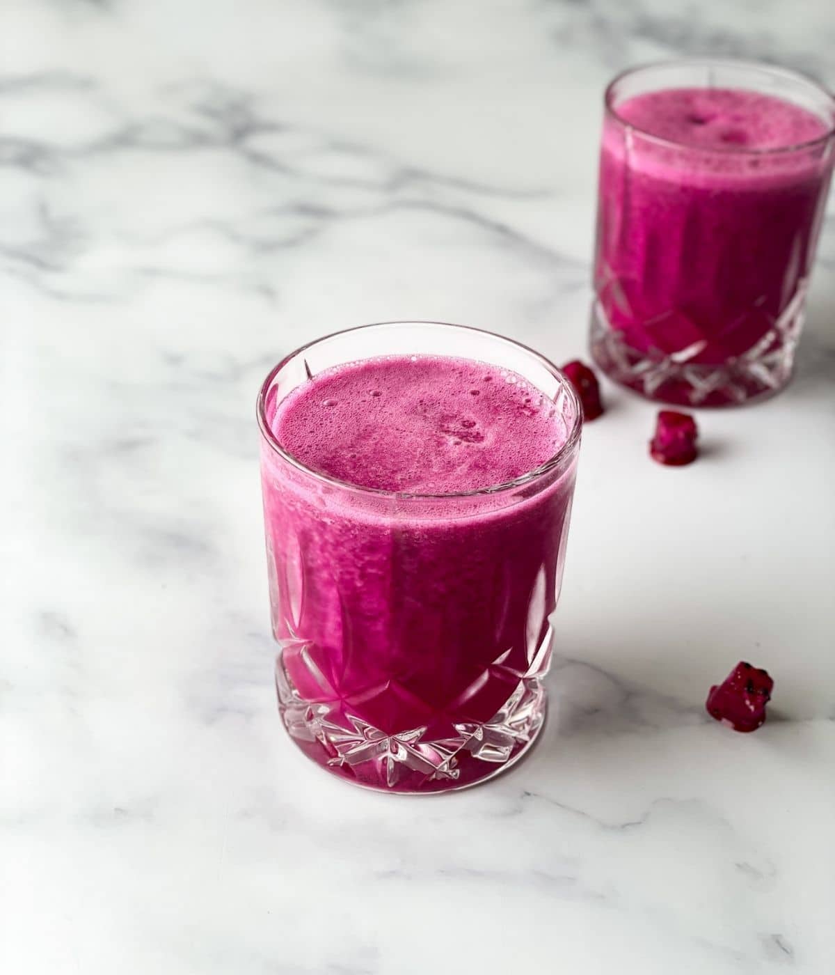 A glass of dragon fruit juice is placed on the white surface.