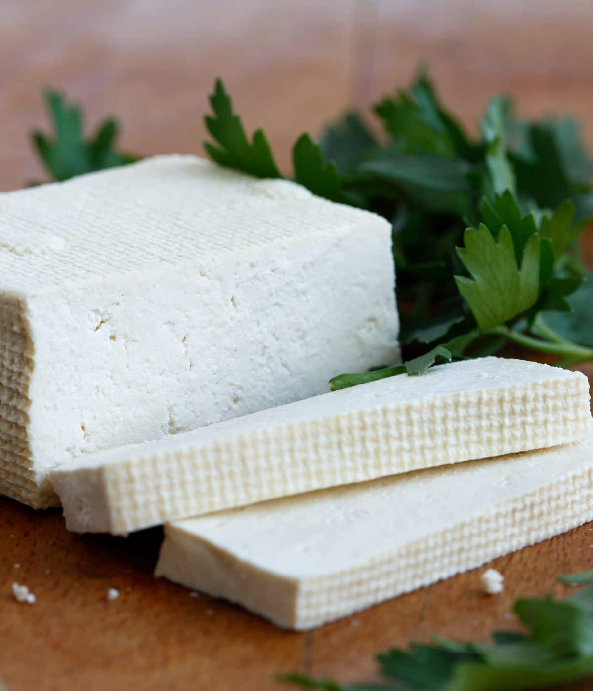 A tofu block is on the cutting board along with parsley. 
