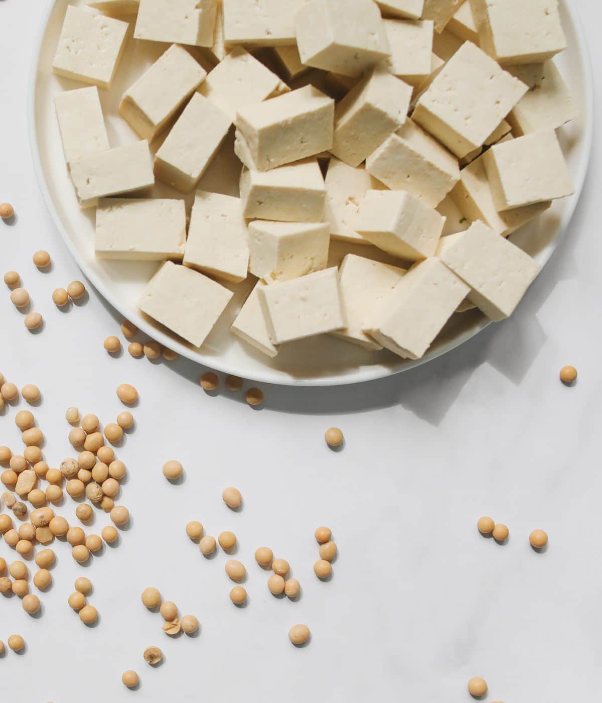 A white plate is with tofu on the table with few soy beans.