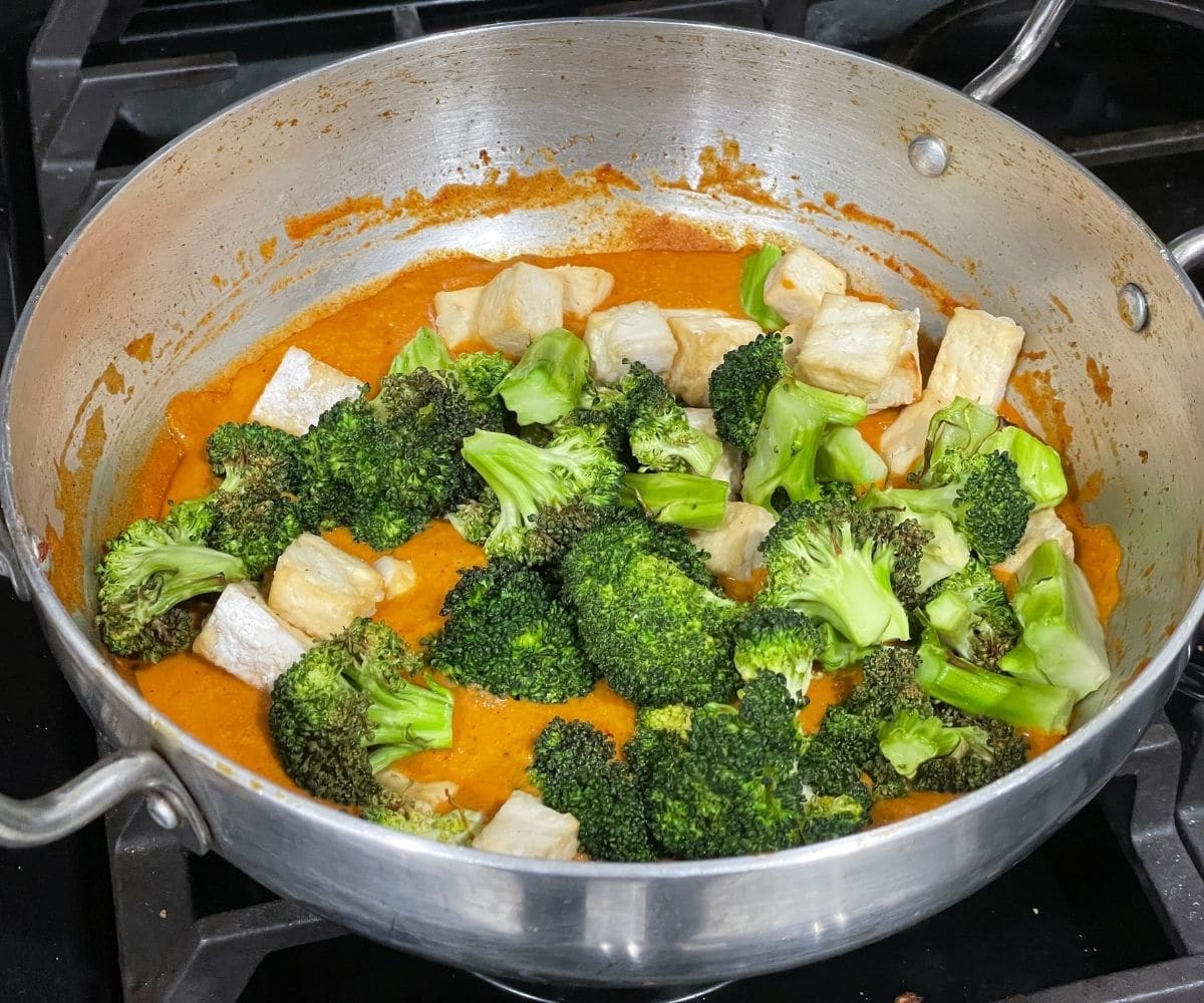 A vessel of broccoli and tofu curry is on the heat.