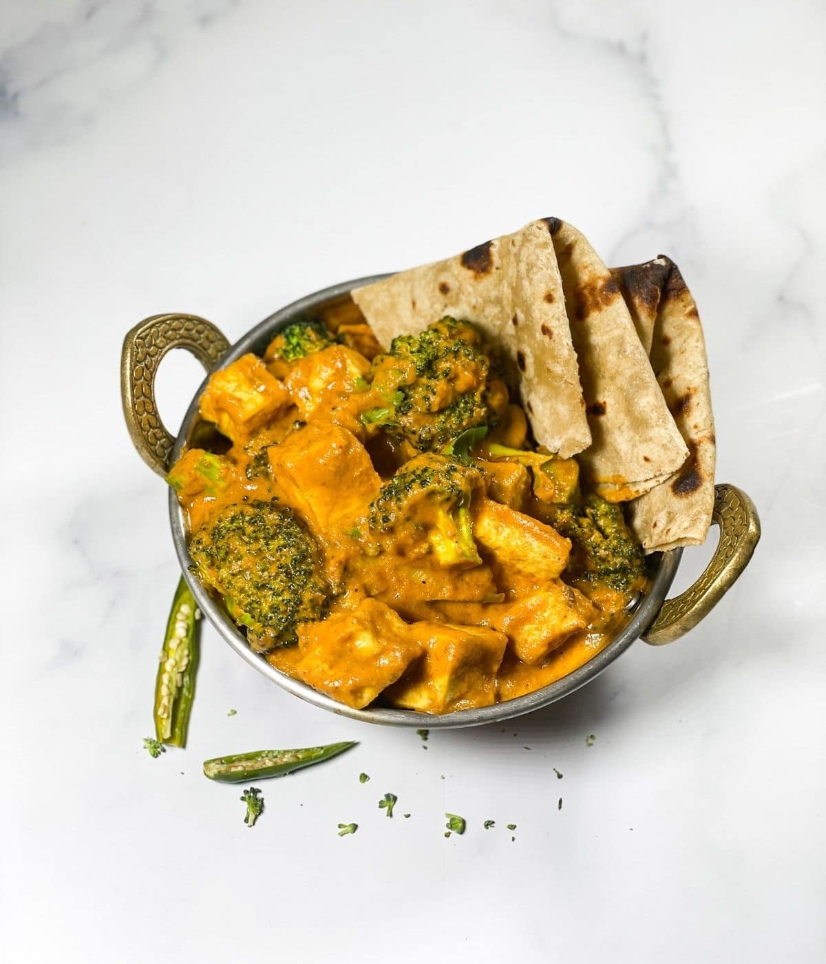 A copper pot is with broccoli tofu curry and roti's.