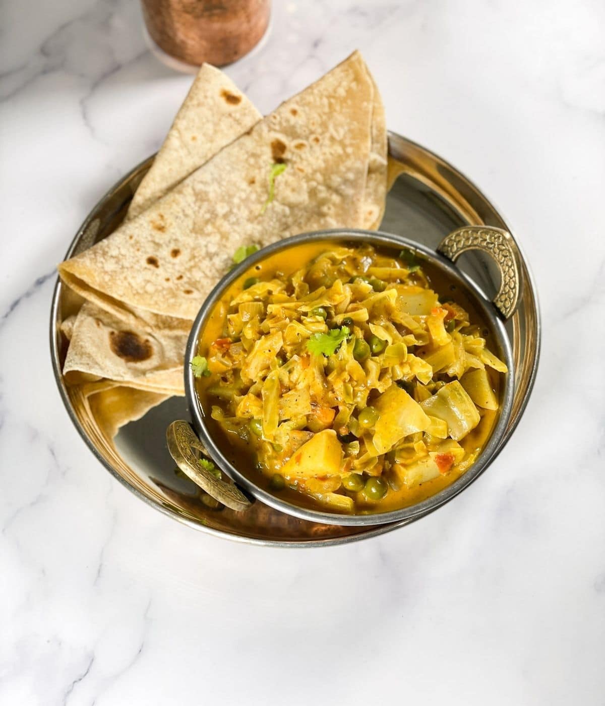 A plate is with bowl of cabbage curry and chapati on the side.