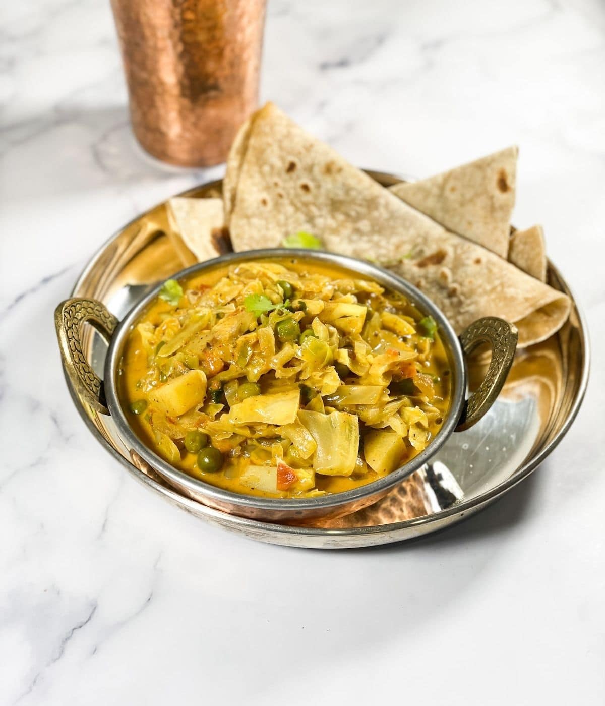 A copper bowl is with cabbage curry along with chapati.