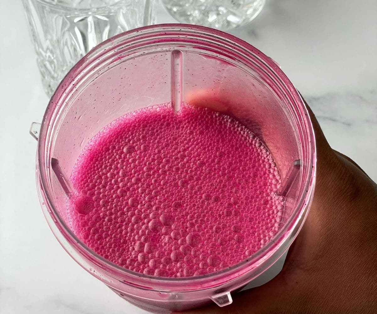 A hand is holding blender filled with dragon fruit juice.