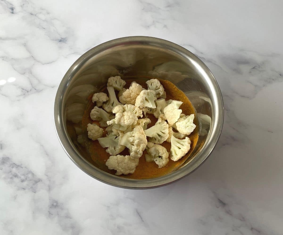 A bowl is with cauliflower and tandoori marinate masala.