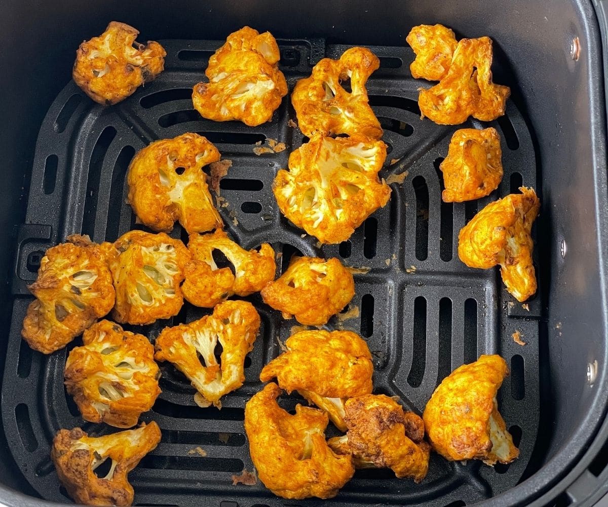 Air fryer basket is with cooked tandoori cauliflower bites.