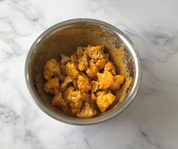 A bowl is with marinated tandoori cauliflower.