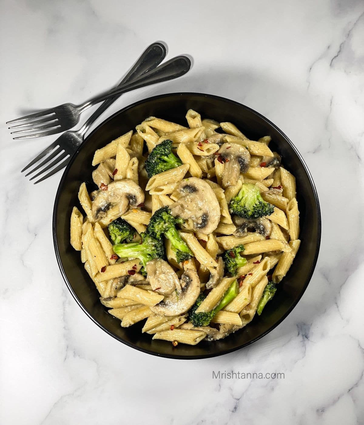 A black bowl is with vegan mushroom and broccoli pasta and fork on side.