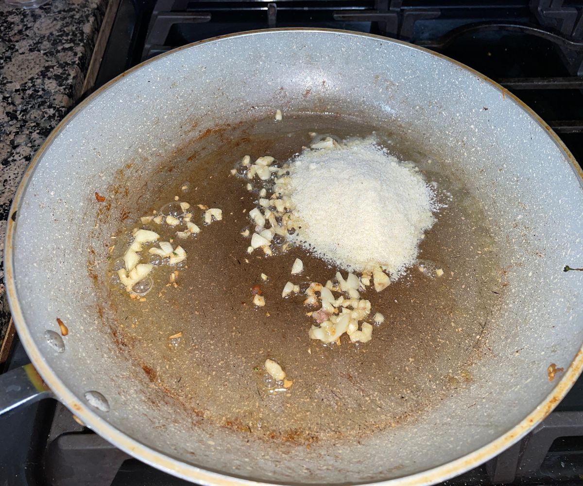 A large pan is with garlic, flour and vegan butter over the stove top.