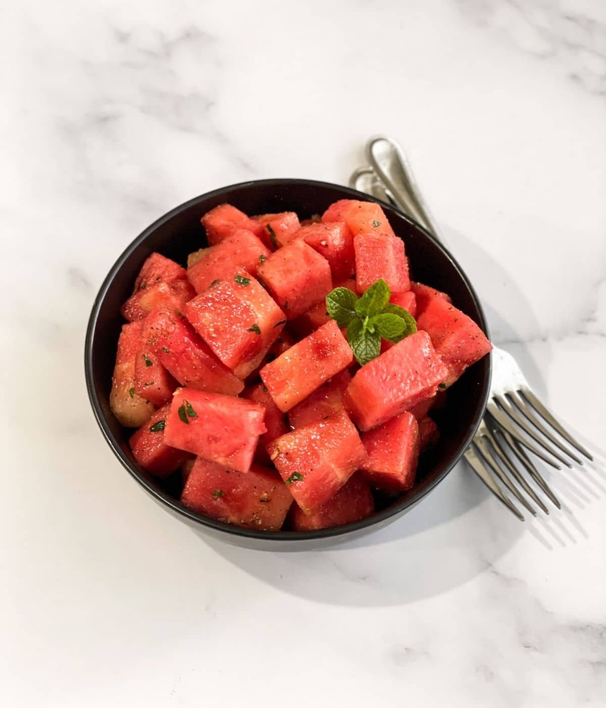 A black bowl is with watermelon chaat and topped with mint leaves.